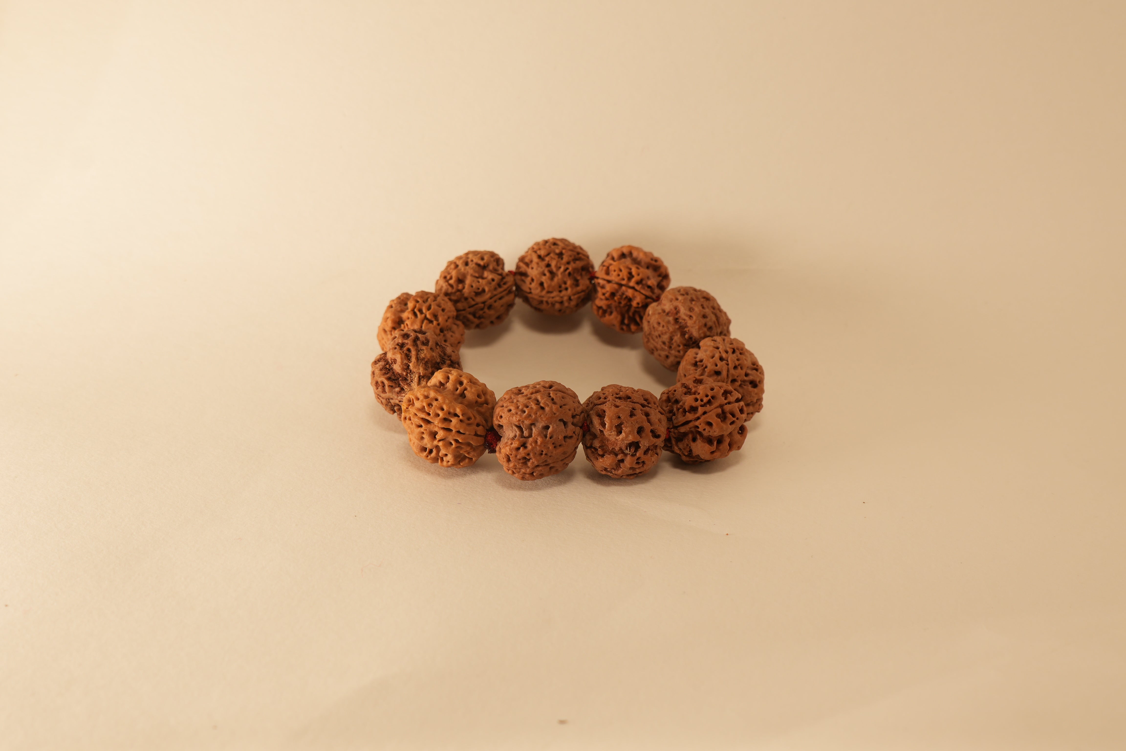 Brown 5 Mukhi Rudraksha beads bracelet with textured natural seed surface on a beige background.